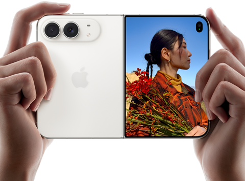 iPhone Duo, couleur blanc stellaire, deux mains le tiennent en orientation horizontale, déplié, le volet gauche montre les deux caméras arrière Fusion 48 mégapixels, le volet droit montre l’écran externe affichant une personne en train de se faire photographier, qui peut se voir pendant la prise grâce à Duo Preview