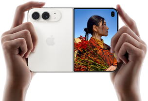 iPhone Duo, couleur blanc stellaire, deux mains le tiennent en orientation horizontale, déplié, le volet gauche montre les deux caméras arrière Fusion 48 mégapixels, le volet droit montre l’écran externe affichant une personne en train de se faire photographier, qui peut se voir pendant la prise grâce à Duo Preview